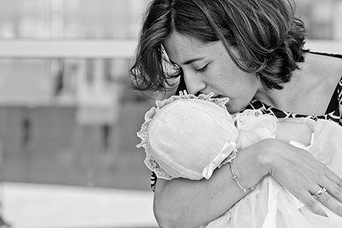 Imagen en blanco y negro de una mujer con su bebé en brazos, le acaba de dar un beso sobre su mejilla, está tomada en exteriores después de realizar el reportaje de bautismo en las Tablas.