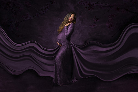 Mujer embarazada en sesión de fotos de estudio, con un vestido morado largo, su cola hace ondas.