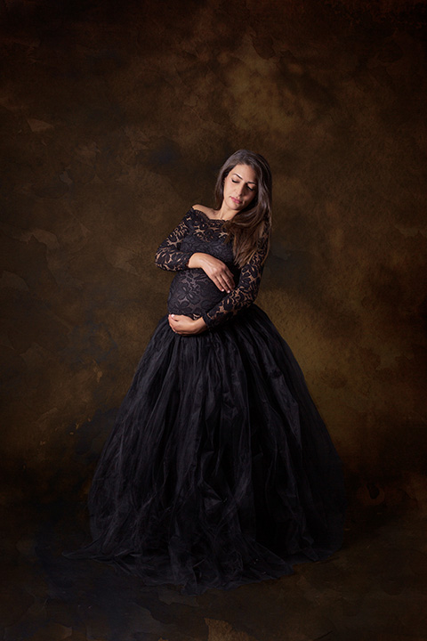 mujer embarazada de pelo largo con una camiseta de encaje y una falda de tul, abrazando su barriga.