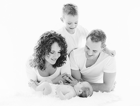 Imagen en blanco y negro de padres con sus dos hijos, están tumbados en el suelo, uno de los hijos abraza a los padres por detrás y el otro es un bebé, sesión realizada por un fotógrafo familiar en Madrid.