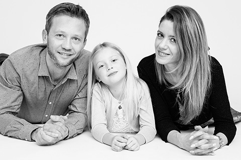 Sesiones de fotos familiares en Madrid realizadas en estudio, imagen en blanco y negro compuesta de padre, madre e hija, tumbados sobre un fondo blanco.