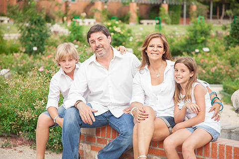 Padre, madre y dos hijos posan en la Rosaleda del parque del Oeste, están sentados y llevan camisas blancas y vaqueros, es una fotografía familiar en Madrid.