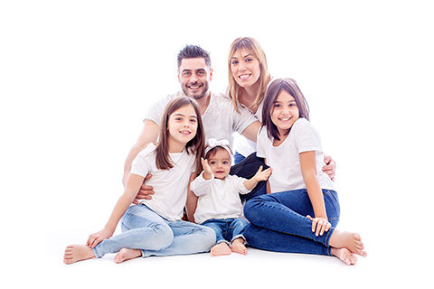 Madre e hijos están sentados sobre un campo de flores blancas y moradas, los niños abrazan a su madre y sonríen, llevan ropa blanca y vaquero, es una fotografía de familia en exteriores.